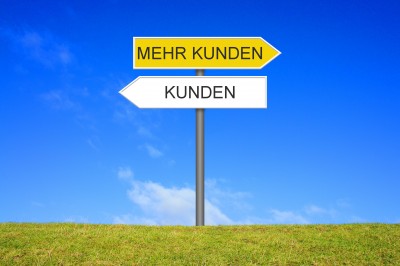 Schild Wegweiser auf einer Wiese zeigt in Richtung Kunden oder Mehr Kunden